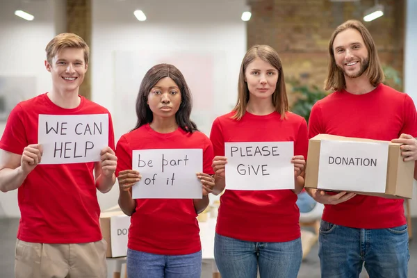 Skupina mladých dobrovolníků s plakáty a dárcovskou krabicí — Stock fotografie