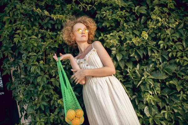 Giovane donna in possesso di una borsa a rete con frutta e cercando premuroso — Foto Stock