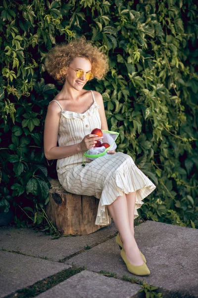 Mujer joven rizada con nectarinas que parecen felices — Foto de Stock
