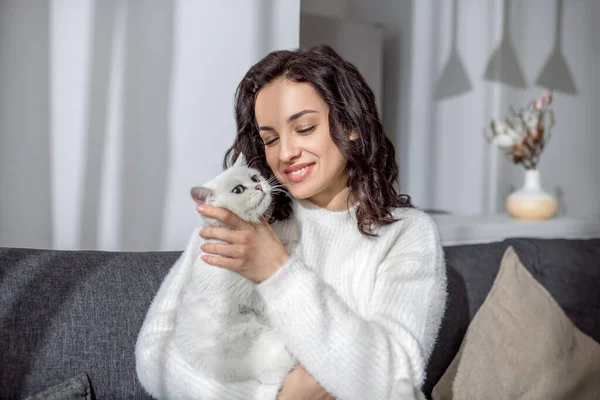 Nette junge Frau sitzt auf dem Sofa und umarmt ihre Katze — Stockfoto