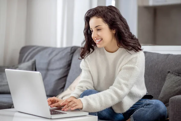 Giovane donna seduta sul divano con un computer portatile e dall'aspetto rilassato — Foto Stock