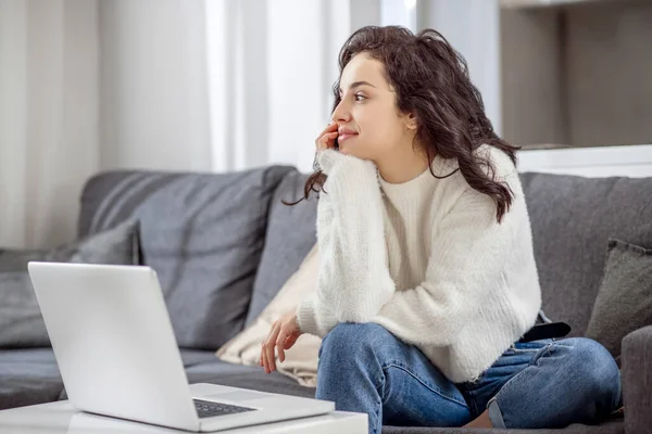 Jovem mulher sentada no sofá com um laptop e olhando relaxado — Fotografia de Stock