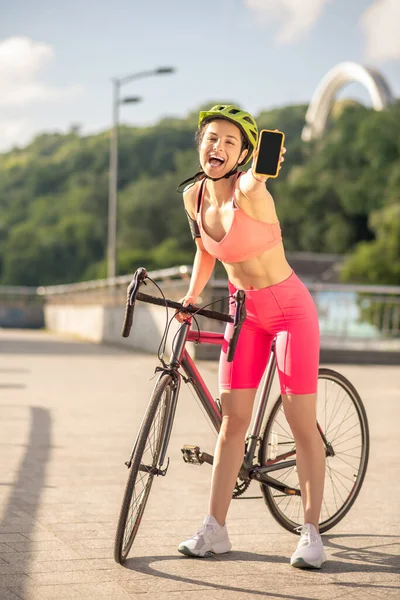 Una chica en ropa de deporte rosa que muestra su teléfono inteligente y se ve emocionada — Foto de Stock