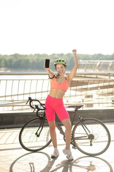 Una chica con una bicicleta de pie en el puente con un smartphone en las manos — Foto de Stock