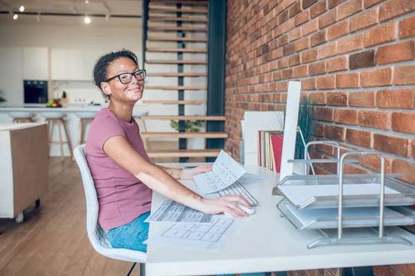 Eine Frau mit Brille arbeitet am Computer und lächelt — Stockfoto