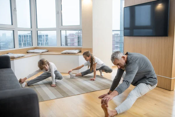 Padre y sus hijos haciendo yoga juntos en casa y estirándose profundamente — Foto de Stock