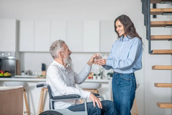 Hombre discapacitado de pelo gris y su joven esposa en la cocina preparando el desayuno — Foto de Stock