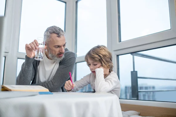 Homme barbu aux cheveux gris assis avec son fils à la table pendant qu'il prend des leçons — Photo