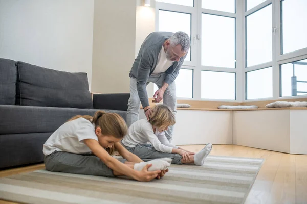 Pai treinando seus filhos em casa fazendo-os esticar corretamente — Fotografia de Stock