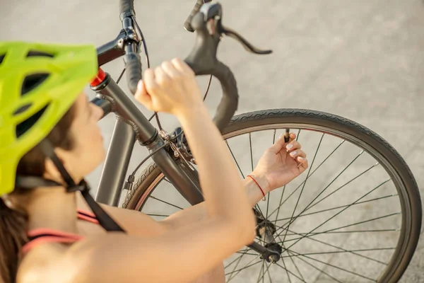 Joven ciclista en ropa deportiva brillante fijando una rueda de bicicleta — Foto de Stock