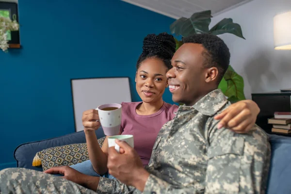 Military and wife drinking coffee on couch