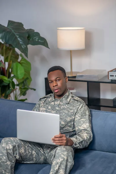 Молодий серйозний військовий чоловік з ноутбуком на дивані — стокове фото