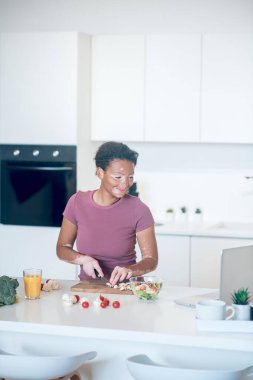 Koyu tenli bir kadın mutfakta yemek pişirirken aynı zamanda bir video bloğu izliyor.