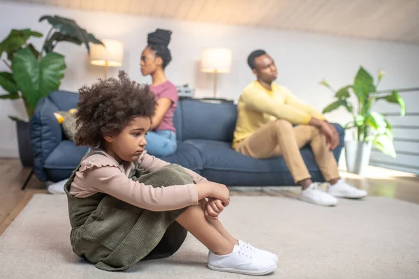 Triste hija en el suelo y padres infelices en el sofá —  Fotos de Stock