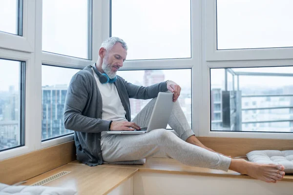 Um homem maduro com um laptop trabalhando em casa e olhando envolvido — Fotografia de Stock
