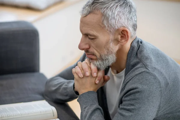 Un hombre de pelo gris sentado con los ojos cerrados y diciendo los pagadores — Foto de Stock