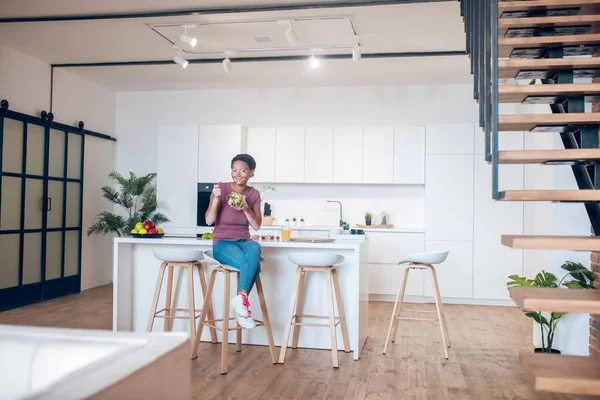 Темнокожая женщина сидит на кухне и ест салат — стоковое фото