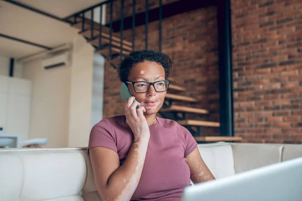 En kvinna i glasögon som arbetar på en bärbar dator och pratar i telefon — Stockfoto