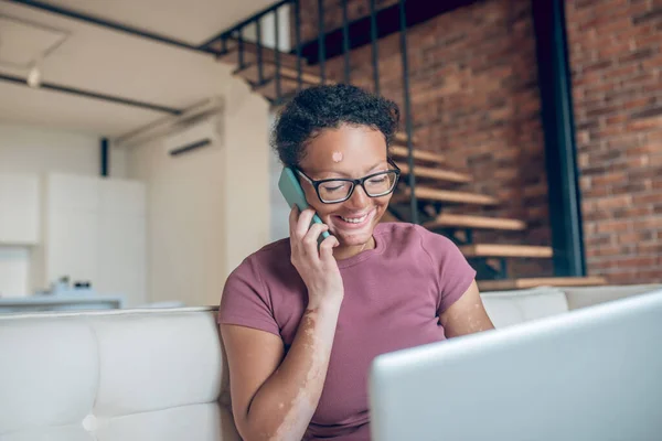 Eine Frau mit Brille arbeitet an einem Laptop und telefoniert — Stockfoto