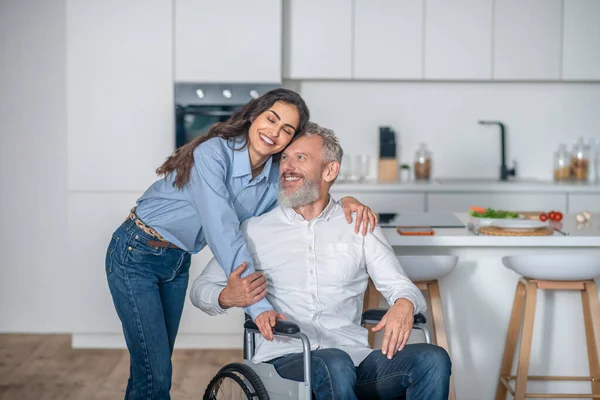 Joven mujer de pelo largo sonriendo amablemente a su discapacitado hausband y ambos mirando feliz — Foto de Stock