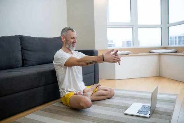 Um homem maduro em tshirt branca sentado no chão e gravando um tutorial de ioga on-line — Fotografia de Stock
