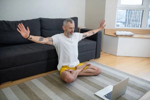 Un hombre maduro en camiseta blanca sentado en el suelo y grabando un tutorial de yoga en línea — Foto de Stock