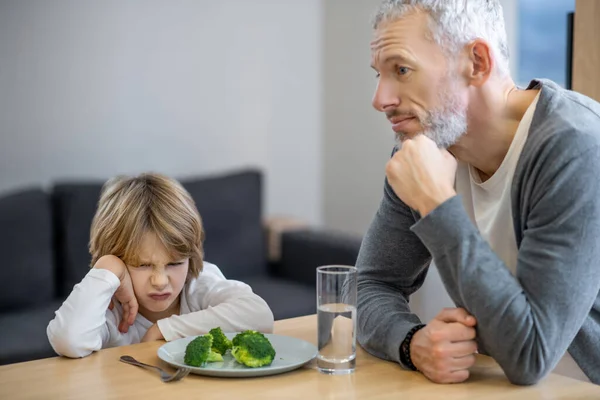 Volwassen man probeert zijn zoon gezond te laten eten terwijl de jongen er ongelukkig uitziet — Stockfoto