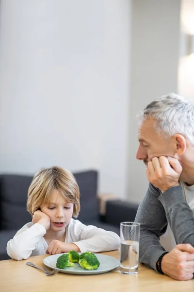 Gammal man försöker få sin son att äta hälsosamt medan pojken ser olycklig ut — Stockfoto