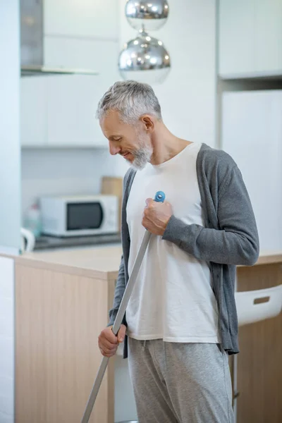 Мужчина в домашней одежде убирает дом и держит швабру — стоковое фото