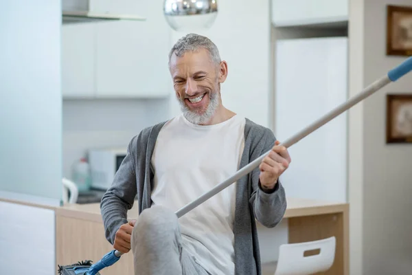 Man in huiskleding die een dweil vasthoudt en een luchtgitaar speelt — Stockfoto