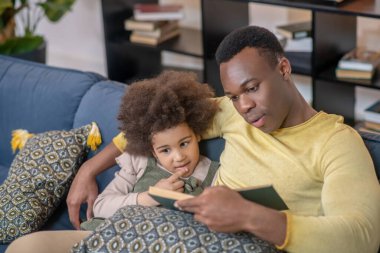 Babası küçük kızına kanepede kitap okuyor.