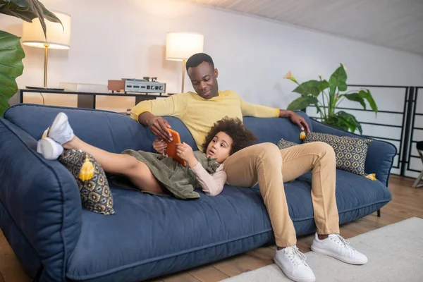 Muž sedí a dcera leží s tabletem na gauči — Stock fotografie