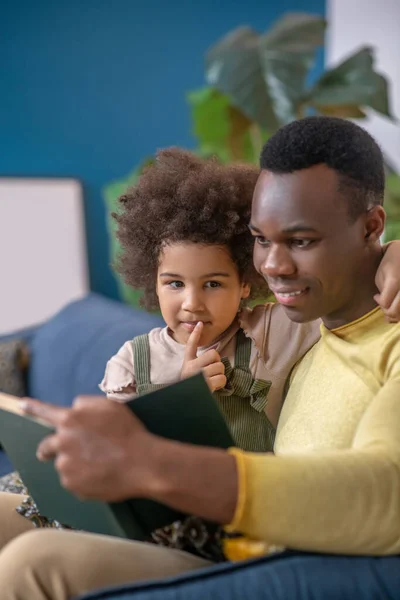 African american reading book to his hugging daughter — 스톡 사진