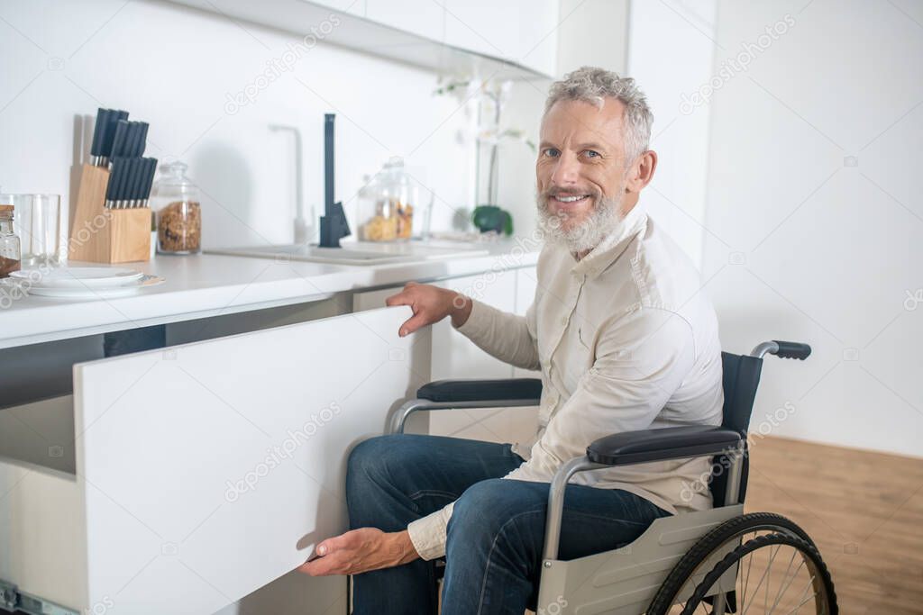 Gray-haired handicapped man in the kitchen smiling nicely