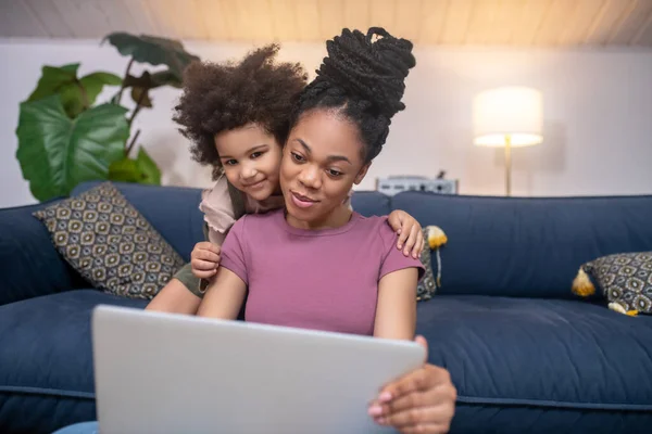Улыбающаяся мама с дочерью смотрит на экран ноутбука — стоковое фото