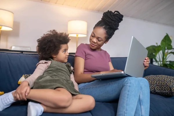 Dizüstü bilgisayarla gülümseyen anne ve sıkılmış küçük kız.