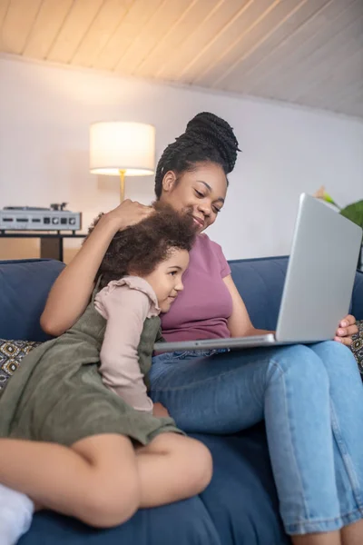 Madre cariñosa abrazando a la pequeña hija mirando a la computadora portátil —  Fotos de Stock