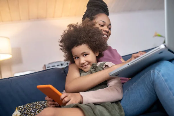 Счастливая темнокожая мама обнимает маленькую дочь планшетом — стоковое фото