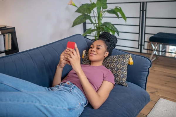 Süße Afroamerikanerin schaut auf Sofa ins Smartphone — Stockfoto