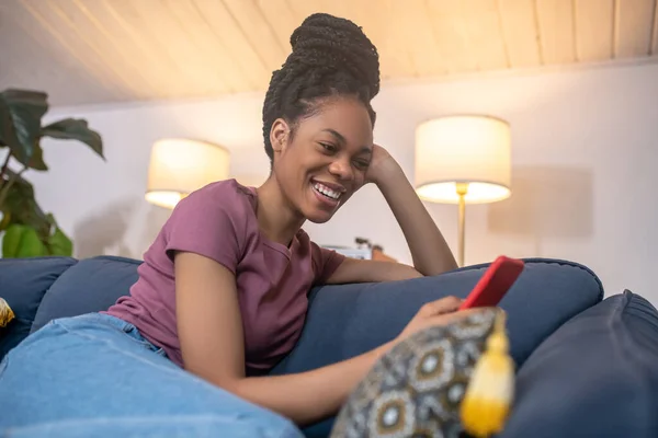 Glada mörkhyade ung kvinna med smartphone på soffan — Stockfoto