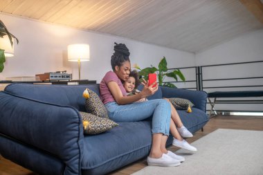 Gülümseyen kadın ve kızı akıllı telefondan selfie çekiyorlar.