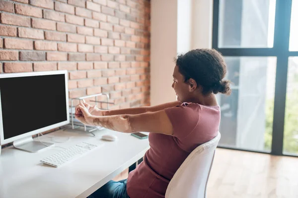 Ung afrikansk amerikansk kvinna sitter vid bordet och stretchar — Stockfoto