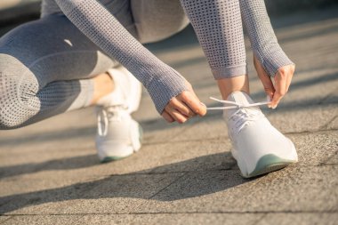 A female in grey sportswear lacing up her snickers