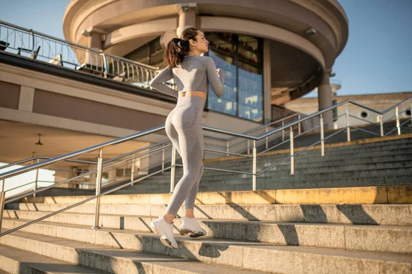 Fit girl in grey sportswear having cardio warm up on the stairs