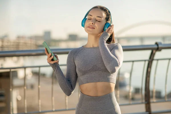 Fit girl in grey sportswear listening to music and looking thoughtful — Fotografia de Stock
