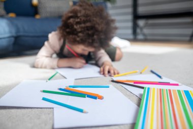 Colored pencils on floor and little girl drawing
