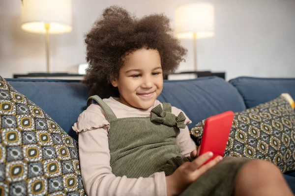 Χαμογελαστό κοριτσάκι με smartphone στον καναπέ — Φωτογραφία Αρχείου