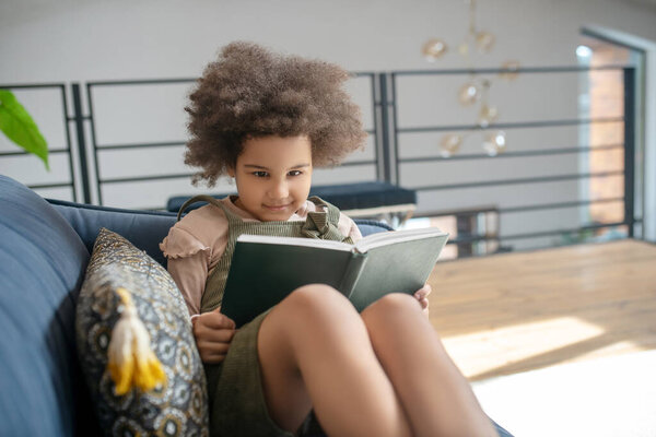 Little smart girl reading book on sofa