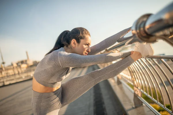 Chica morena en ropa deportiva gris entrenando su flexibilidad — Foto de Stock