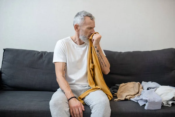 Šedovlasý muž, který vypadá nešťastně, zatímco přemýšlí o praní oblečení. — Stock fotografie